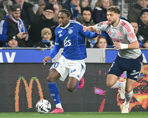 Piłkarz RC Strasbourg w niebieskiej koszulce z numerem 20 walczy o piłkę z zawodnikiem Olympique Lyon.