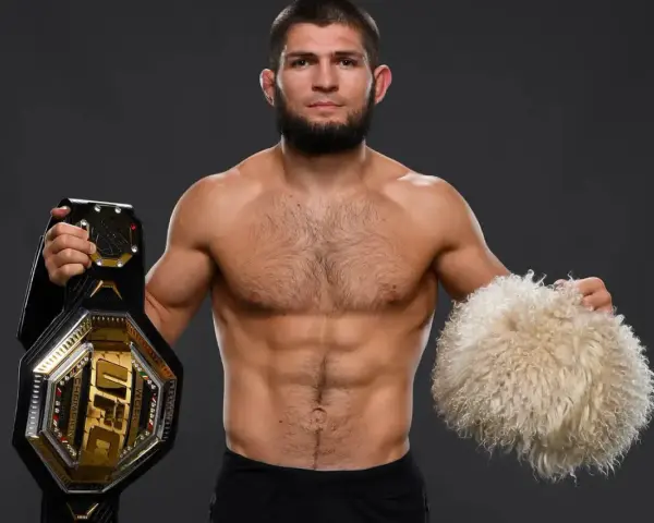 Khabib Nurmagomedov, jeden z najlepsi zawodnicy mma w historii, prezentuje pas UFC i tradycyjną czapkę.