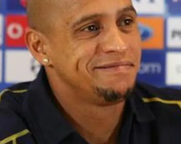 Roberto Carlos, znany z prowadzenia drużyn, w ciemnej koszulce z żółtymi akcentami, na tle z logo PlayStation.