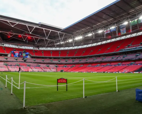 Pusta trybuna stadionu Wembley, który jest największym stadionem na świecie, z zieloną murawą i czerwonymi siedzeniami.