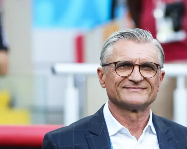 Uśmiechnięty mężczyzna w okularach, były trener reprezentacji Polski, w garniturze i białej koszuli.