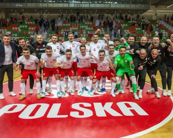 Drużyna Polski świętuje sukces na futsalowych mistrzostwach świata. Piłkarze w biało-czerwonych strojach z dumą pozują na tle napisu "POLSKA".