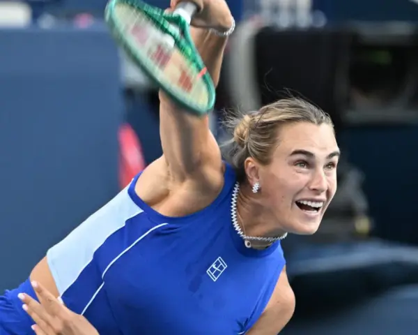 Aryna Sabalenka w akcji, z rakietą w górze, gotowa do serwisu. Widać jej skupienie i determinację, kiedy gra Sabalenka.