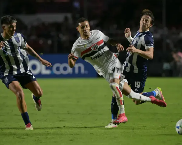 Piłkarze walczą o piłkę na boisku, jeden z nich w białej koszulce z logo São Paulo FC, walcząc o wysokie rankingi.