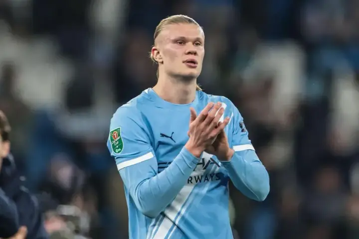 Erling Haaland w błękitnej koszulce Manchesteru City, z dłońmi złożonymi w geście uznania.