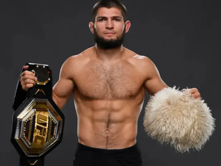 Khabib Nurmagomedov, jeden z najlepsi zawodnicy mma w historii, prezentuje pas UFC i tradycyjną czapkę.