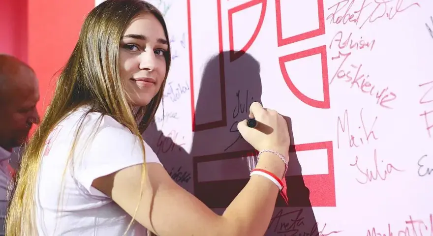 Julia Szeremeta pisze swoje imię na białej ścianie z czerwonymi elementami.