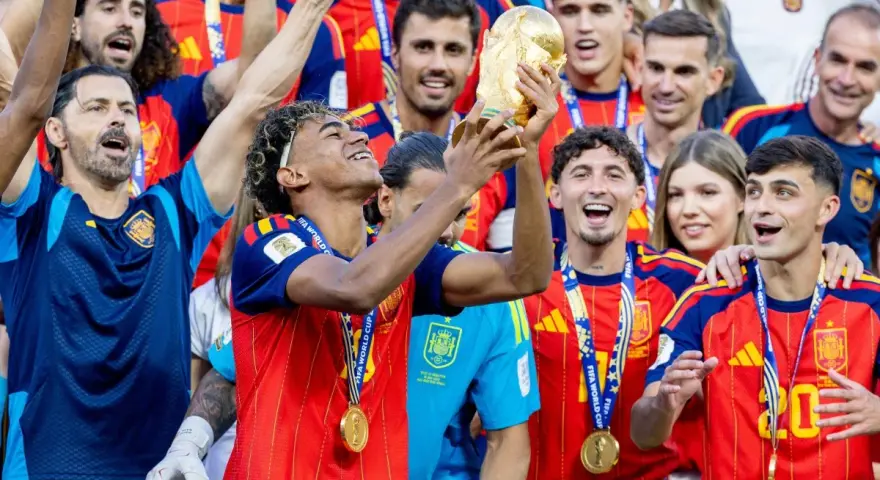 Radość reprezentacji Hiszpanii w piłce nożnej mężczyzn po zdobyciu pucharu. Piłkarze w złotych medalach i czerwonych koszulkach świętują z trofeum.