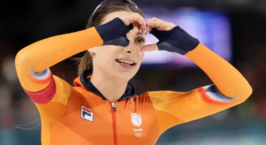 Femke Kok w pomarańczowym stroju TeamNL tworzy serce dłońmi, patrząc przez nie z uśmiechem.