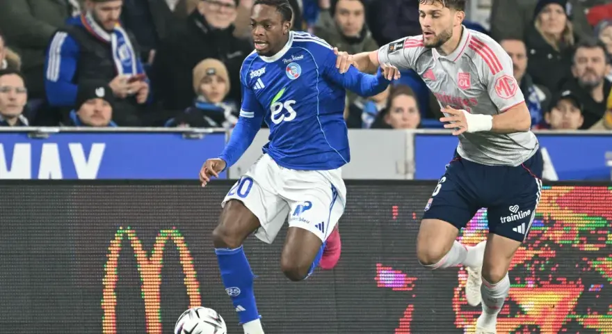 Piłkarz RC Strasbourg w niebieskiej koszulce z numerem 20 walczy o piłkę z zawodnikiem Olympique Lyon.