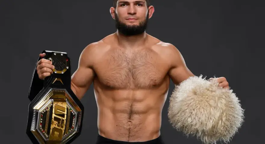 Khabib Nurmagomedov, jeden z najlepsi zawodnicy mma w historii, prezentuje pas UFC i tradycyjną czapkę.