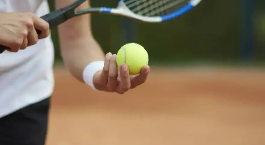 Gracz trzyma piłkę tenisową, gotowy do serwisu. To moment, w którym można zdobyć przewagę w tenisie.