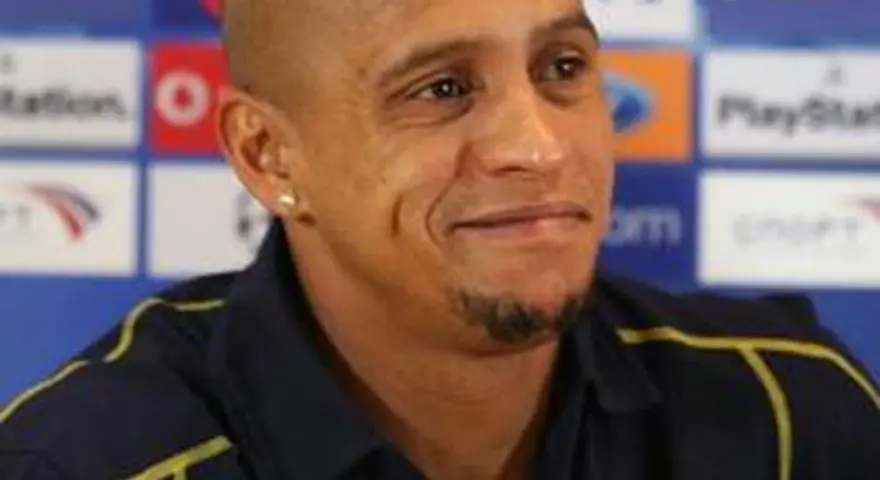 Roberto Carlos, znany z prowadzenia drużyn, w ciemnej koszulce z żółtymi akcentami, na tle z logo PlayStation.