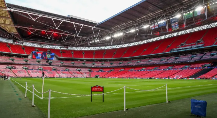 Pusta trybuna stadionu Wembley, który jest największym stadionem na świecie, z zieloną murawą i czerwonymi siedzeniami.