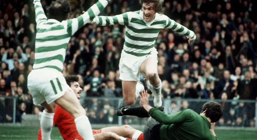 Futboliści z Glasgow w zielono-białych pasach świętują zwycięstwo, jeden z nich przeskakuje nad leżącym przeciwnikiem.