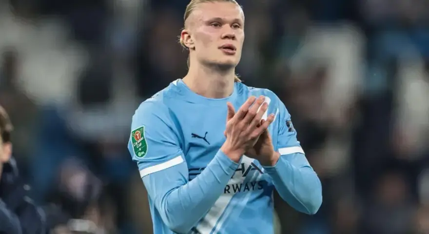Erling Haaland w błękitnej koszulce Manchesteru City, z dłońmi złożonymi w geście uznania.