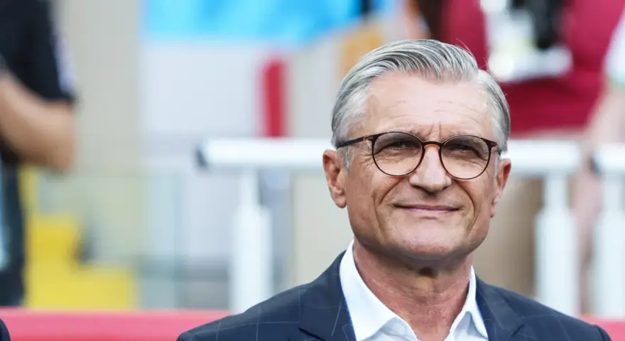 Uśmiechnięty mężczyzna w okularach, były trener reprezentacji Polski, w garniturze i białej koszuli.