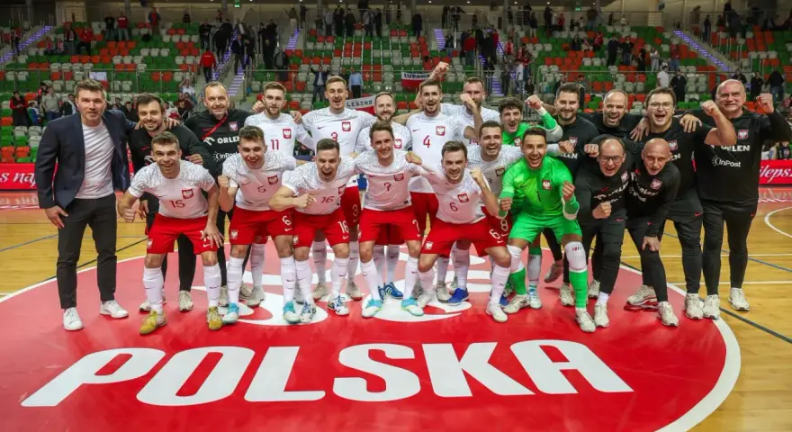 Drużyna Polski świętuje sukces na futsalowych mistrzostwach świata. Piłkarze w biało-czerwonych strojach z dumą pozują na tle napisu "POLSKA".