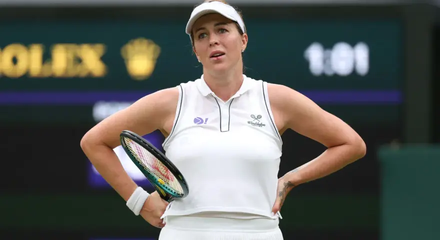 Anastasija Pawluczenkowa z rakietą, w białej koszulce Wimbledonu, zamyślona na korcie.