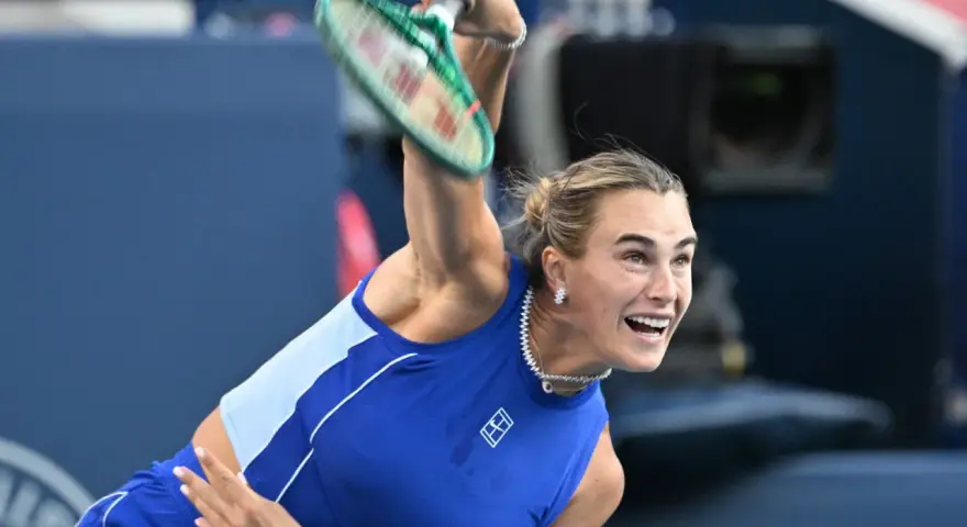 Aryna Sabalenka w akcji, z rakietą w górze, gotowa do serwisu. Widać jej skupienie i determinację, kiedy gra Sabalenka.