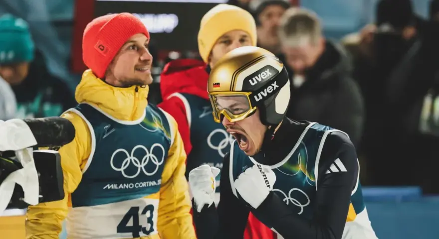 Philipp Raimund w złoto-czarnym kasku i goglach krzyczy z radości, obok kolega w czerwonej czapce i żółtej kurtce.