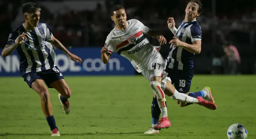 Piłkarze walczą o piłkę na boisku, jeden z nich w białej koszulce z logo São Paulo FC, walcząc o wysokie rankingi.