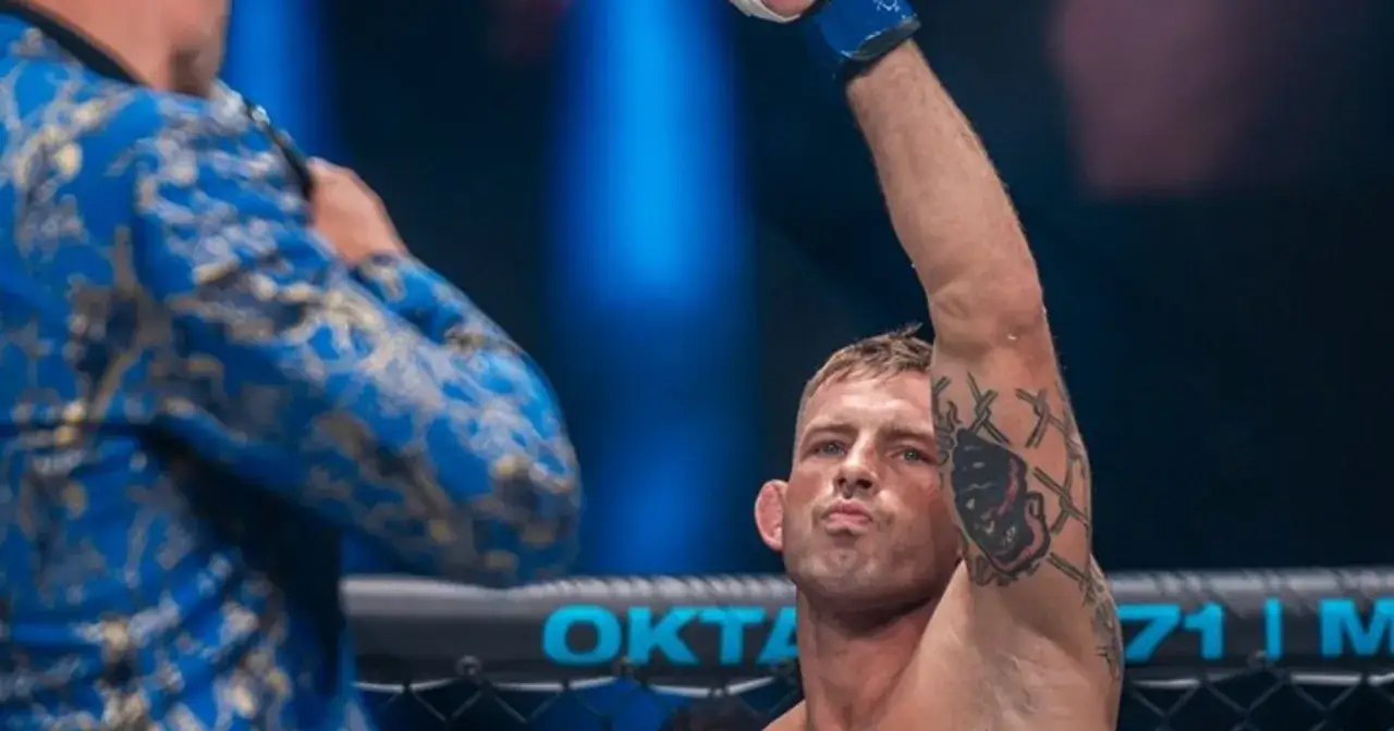 Polscy mma zawodnicy: wojownik z tatuażem na ramieniu unosi rękę w geście triumfu, obok niego stoi trener w niebieskiej, złotej marynarce.