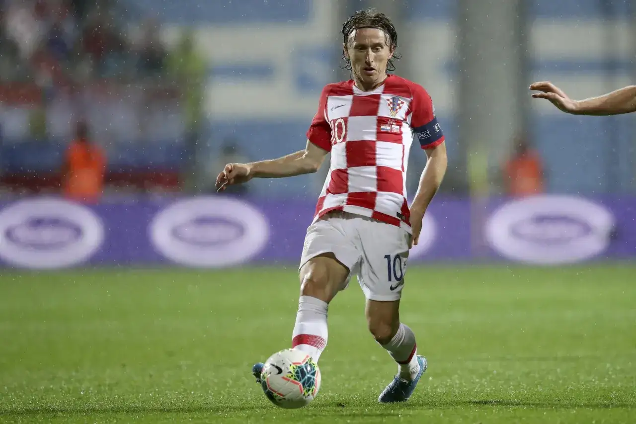 Piłkarz w koszulce Chorwacji z numerem 10, Luka Modrić, drybluje w deszczu. Ile lat ma Luka Modrić? Wciąż w formie!