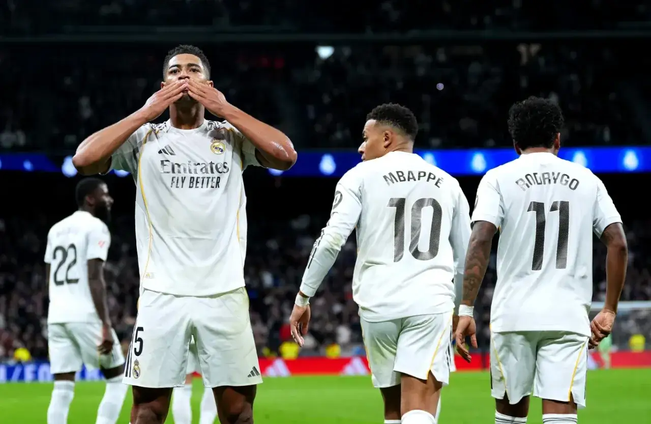 Piłkarze Realu Madryt świętują zwycięstwo nad Sevillą FC. Na pierwszym planie zawodnik z numerem 5 całuje dłonie. W tle widać graczy z numerami 10 (Mbappe) i 11 (Rodrygo).