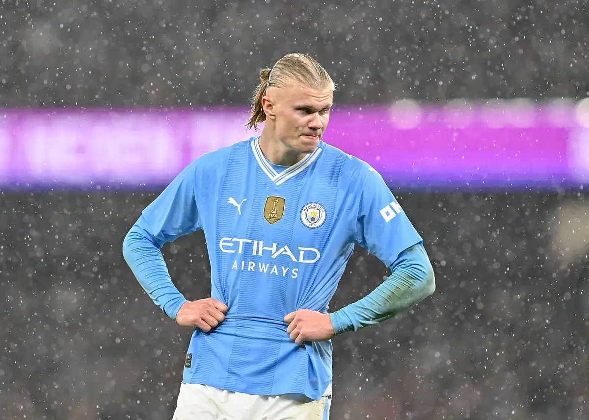 Erling Haaland w błękitnej koszulce Manchesteru City, z rękami na biodrach, w deszczu.