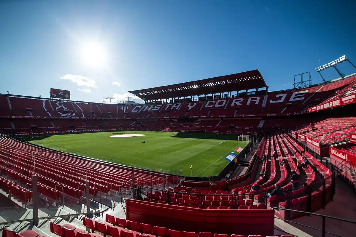 Puste trybuny stadionu Ramón Sánchez Pizjuán przed meczem Sevilla FC. Słońce świeci nad boiskiem, zapowiadając emocjonujące rozgrywki.