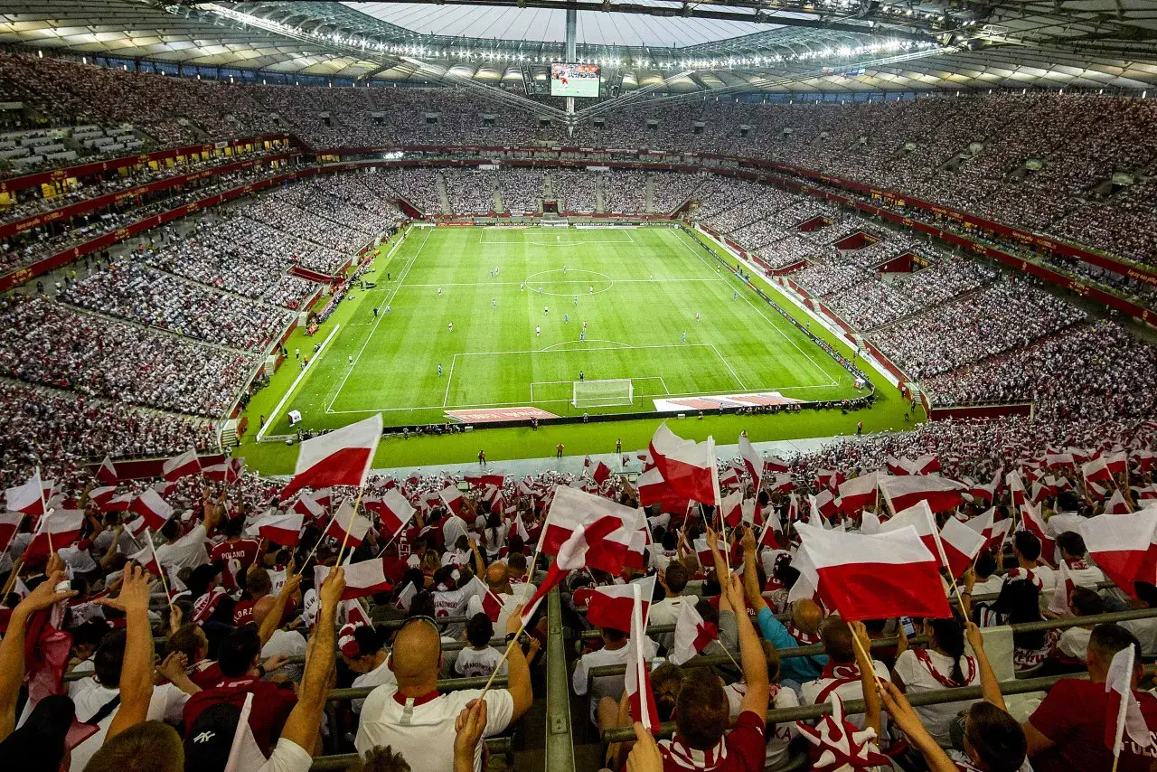 Tysiące kibiców z polskimi flagami na trybunach stadionu, gotowi do dopingu podczas meczów reprezentacji Polski w 2025 roku.