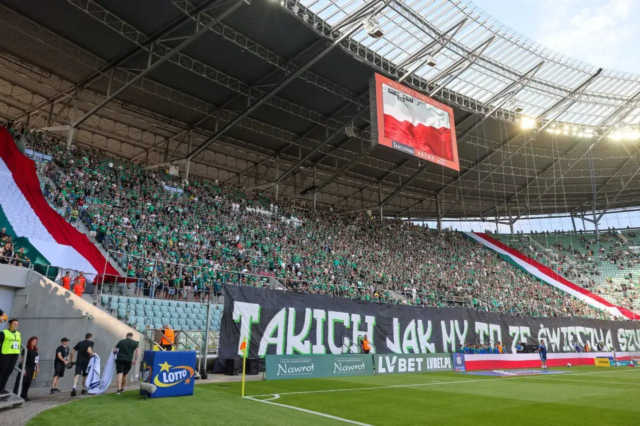 Trybuny stadionu wypełnione kibicami Śląska Wrocław. Rozgrywki w pełni, fani tworzą niesamowitą atmosferę.