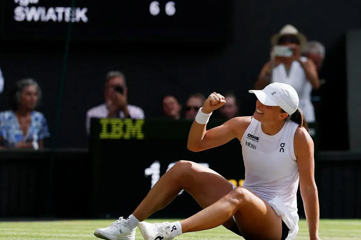 Iga Świątek świętuje zwycięstwo na Wimbledonie, siedząc na trawie i unosząc zaciśniętą pięść w geście triumfu.