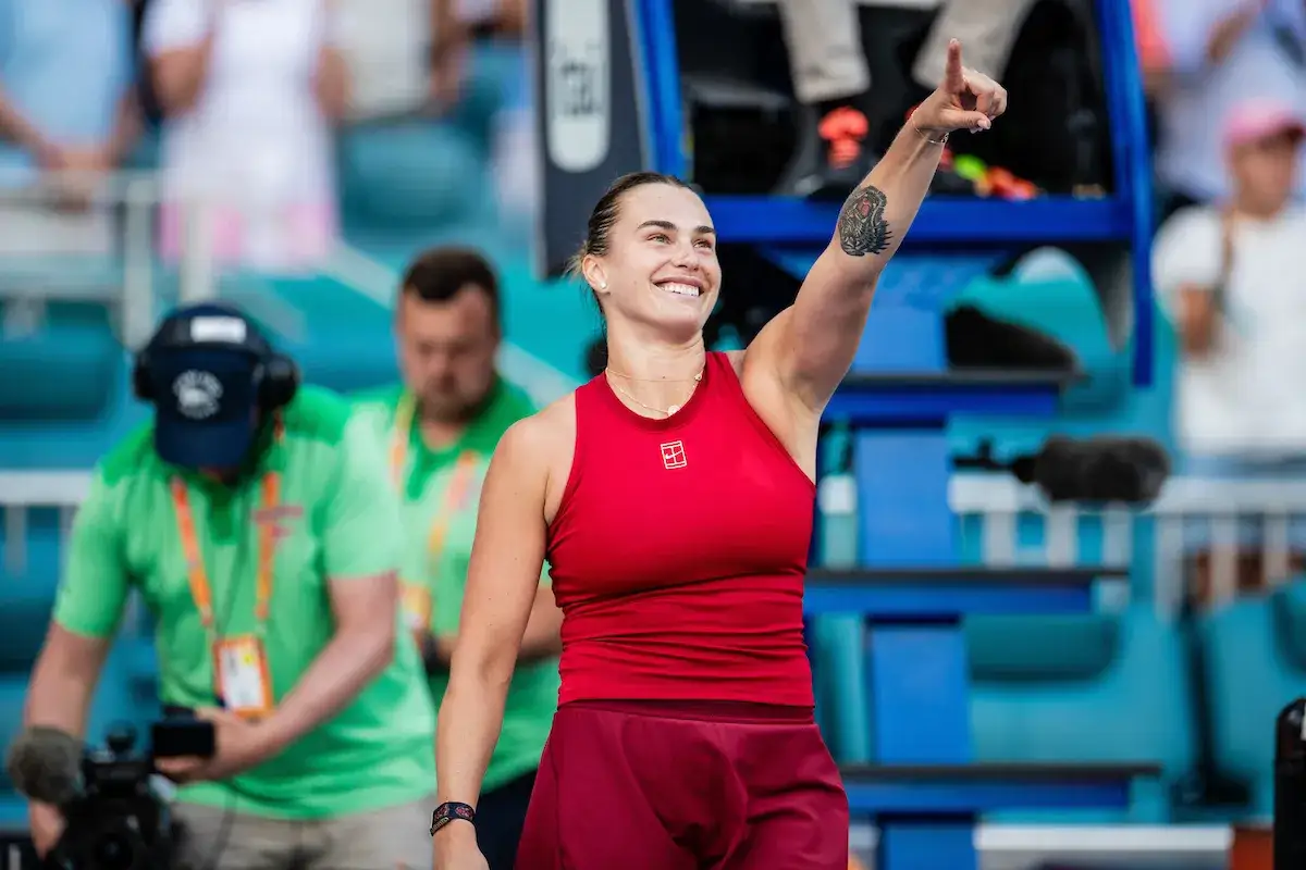 Uśmiechnięta Sabalenka w czerwonym stroju, z podniesionym palcem, jakby mówiła