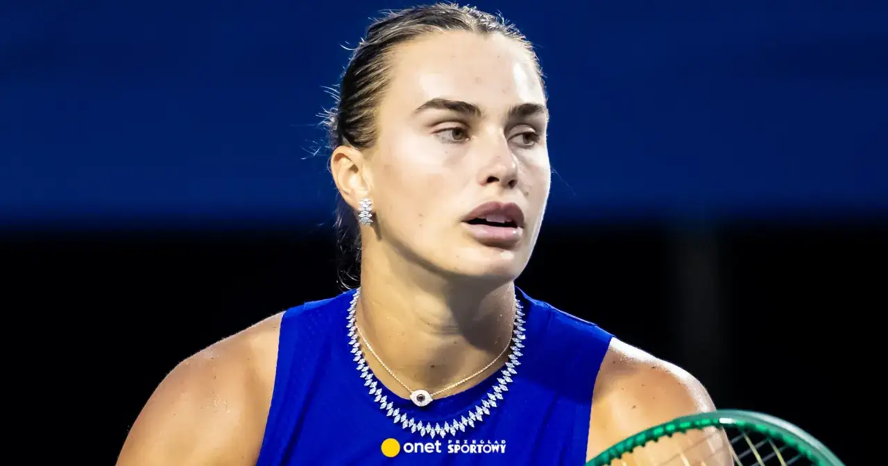 Aryna Sabalenka w błyszczącej biżuterii i niebieskiej koszulce, gotowa do gry.
