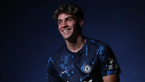 Uśmiechnięty Marc Guiu w ciemnogranatowej koszulce Chelsea z niebieskimi wzorami.